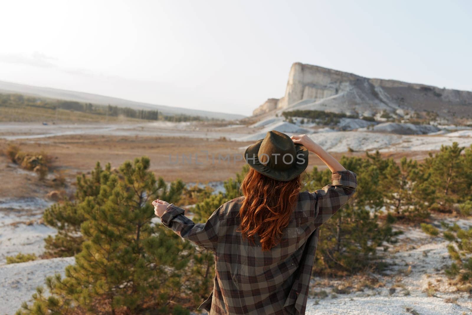 Woman in plaid shirt and hat gazing at majestic mountain view in the distance