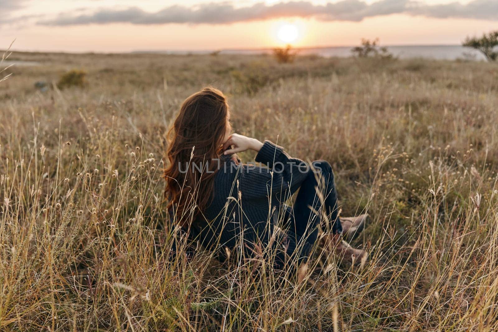 Serene woman watching sunset in peaceful field, contemplating the beauty of nature