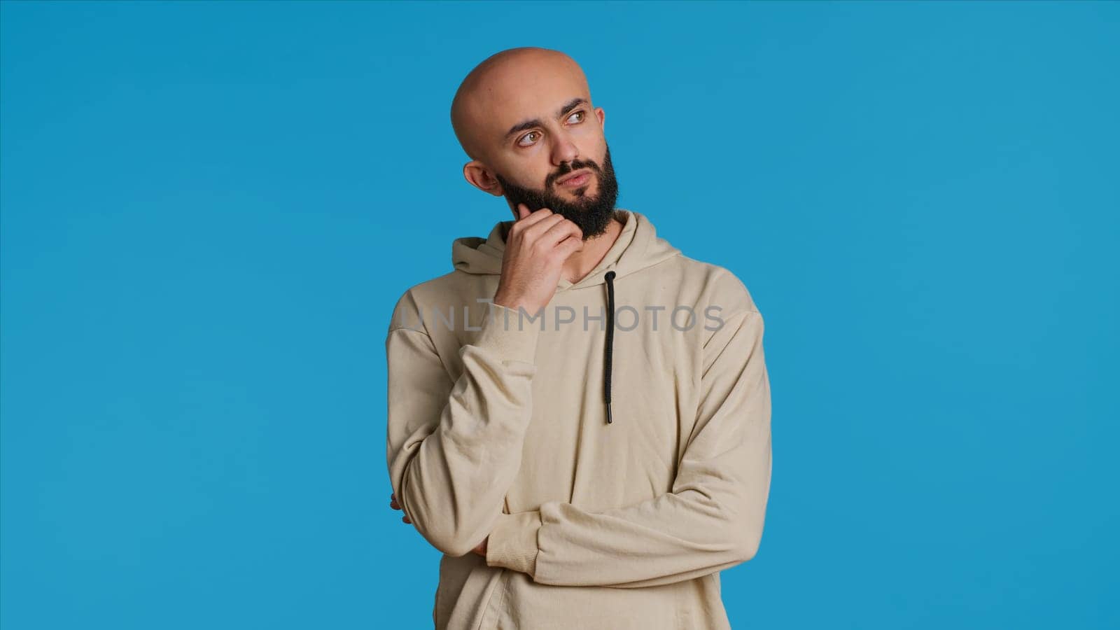 Thoughtful person being puzzled about a decision, standing over blue background in studio and thinking. Pensive middle eastern man being uncertain and doubtful about something. Camera 1.