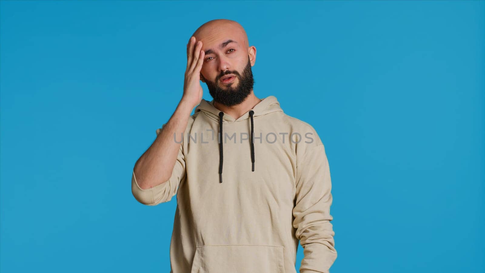 Muslim man suffering from serious migraine on camera, trying to rub temples to ease the pressure. Young middle eastern adult feeling unwell with painful headache, sick person. Camera 1.