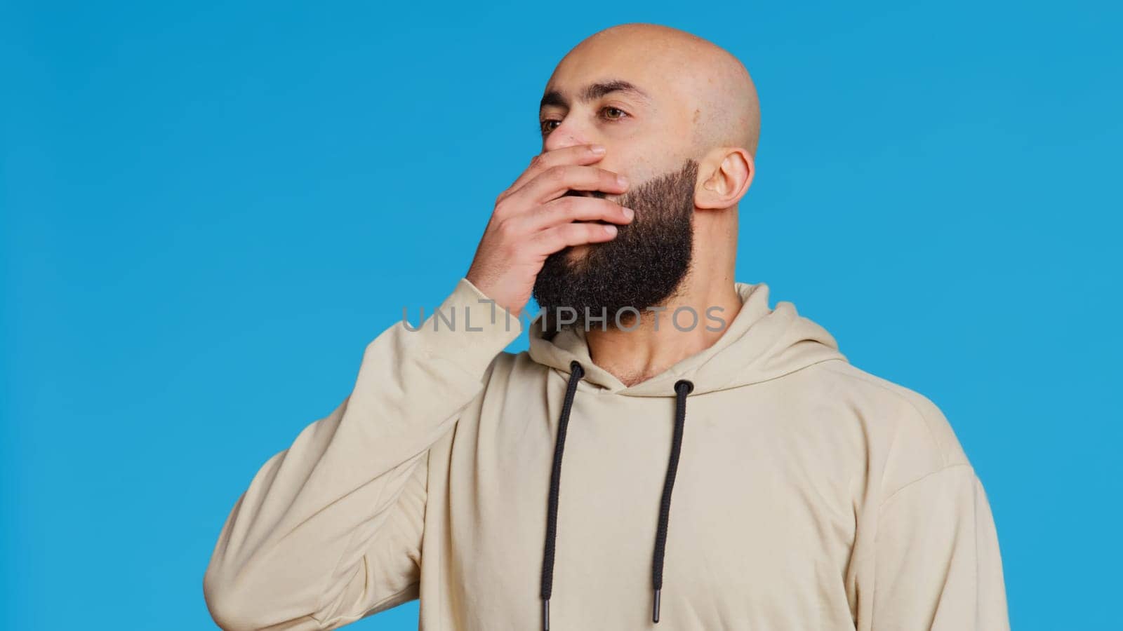 Middle eastern man feeling exhausted and yawning in studio, covering his mouth in front of the camera. Arab person being sleepy in the morning, awake from the early hours. Camera 2.