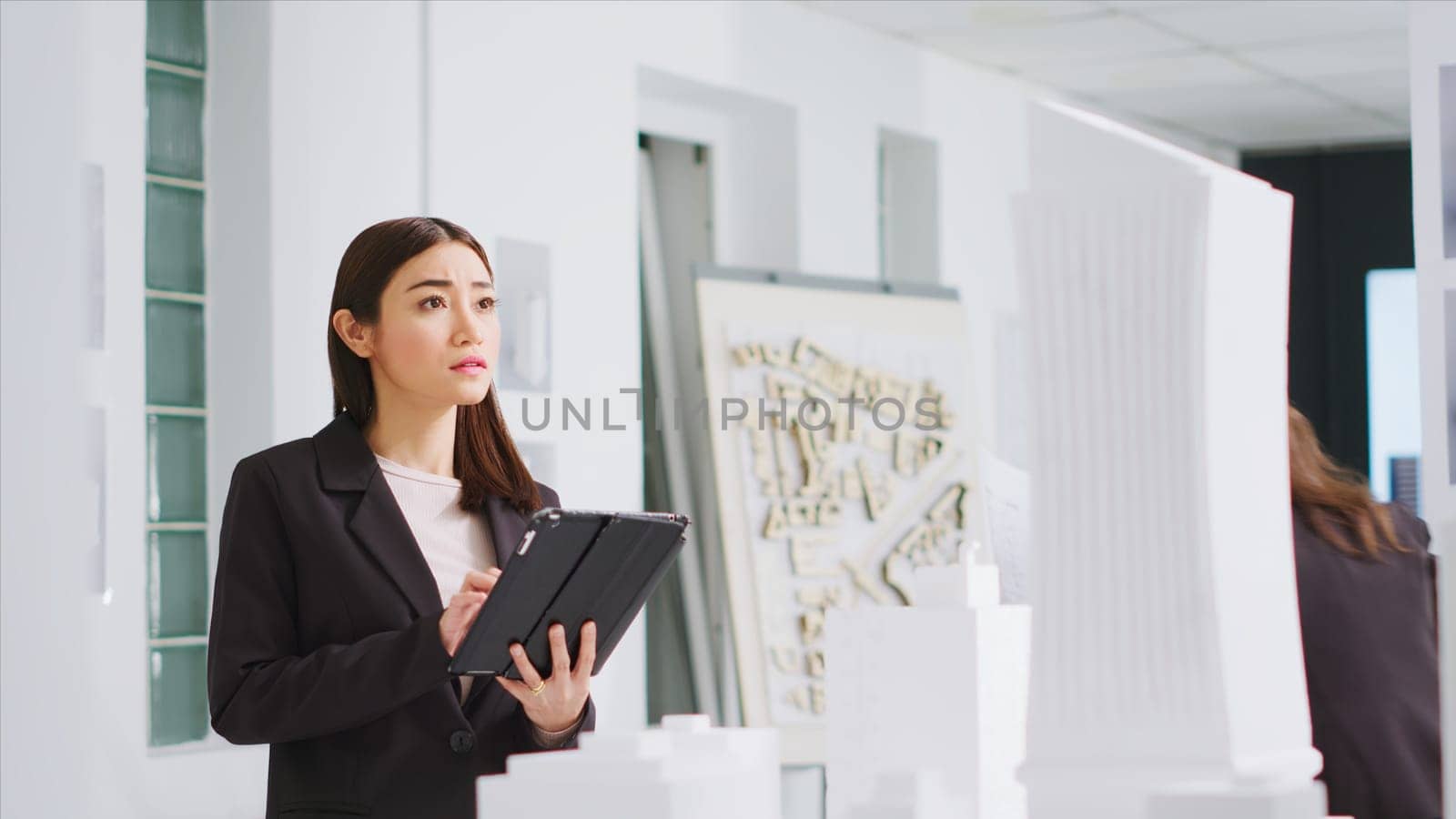 In property management office, contractor uses tablet to evaluate and estimate variables as they work with 3D printed architectural prototype. Engineer working to design urban area with housing.