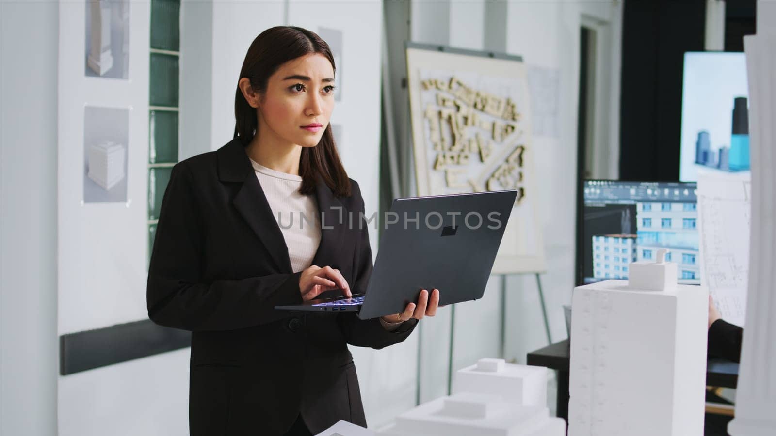 Real estate agency worker measuring printed building maquette at manufacturing office, looks at property sketch on laptop. Woman architect taking notes of scale elements for residential area layout.