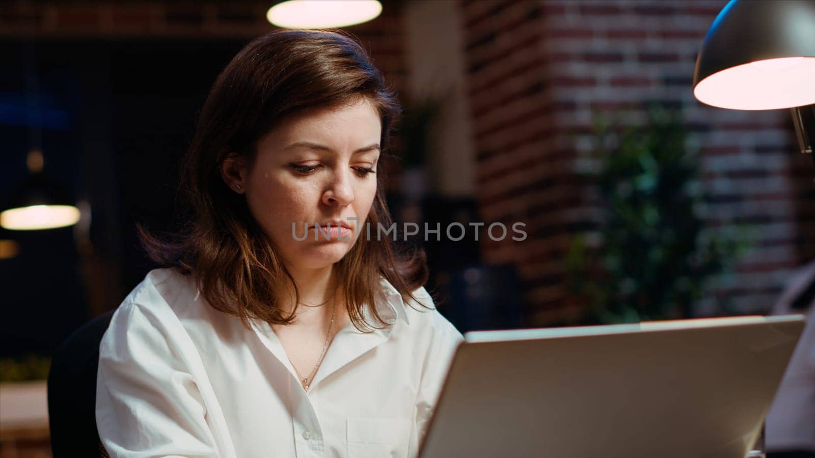 Businesswoman researching key data for company project, doing tasks in office overnight. Employee looking over accounting figures on laptop screen late at night, typing on keyboard, camera B