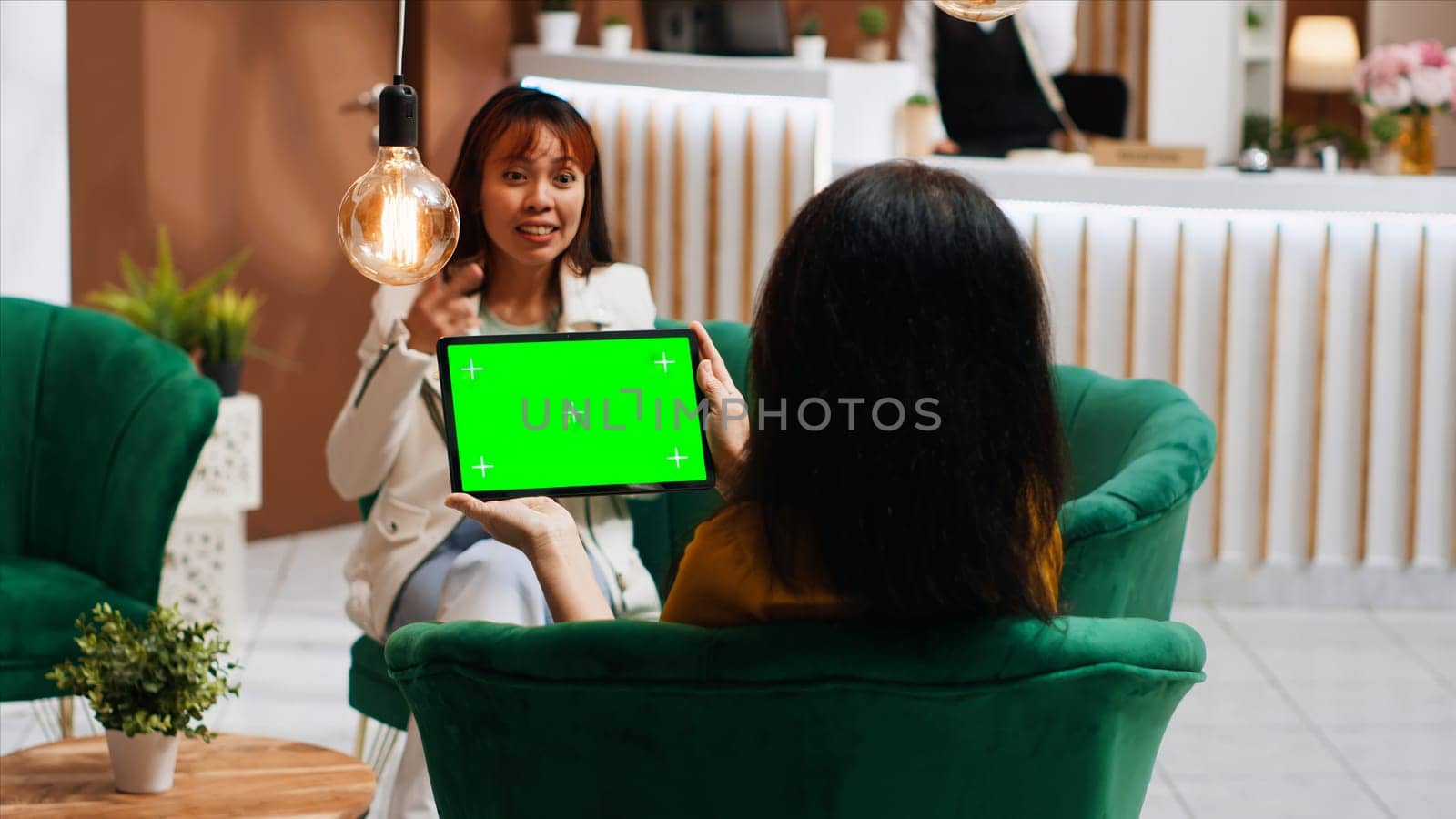 Hotel guest holding tablet with greenscreen layout in lobby, looking at chromakey isolated display and relaxing on sofa. Woman checking blank mockup copyspace screen on gadget.