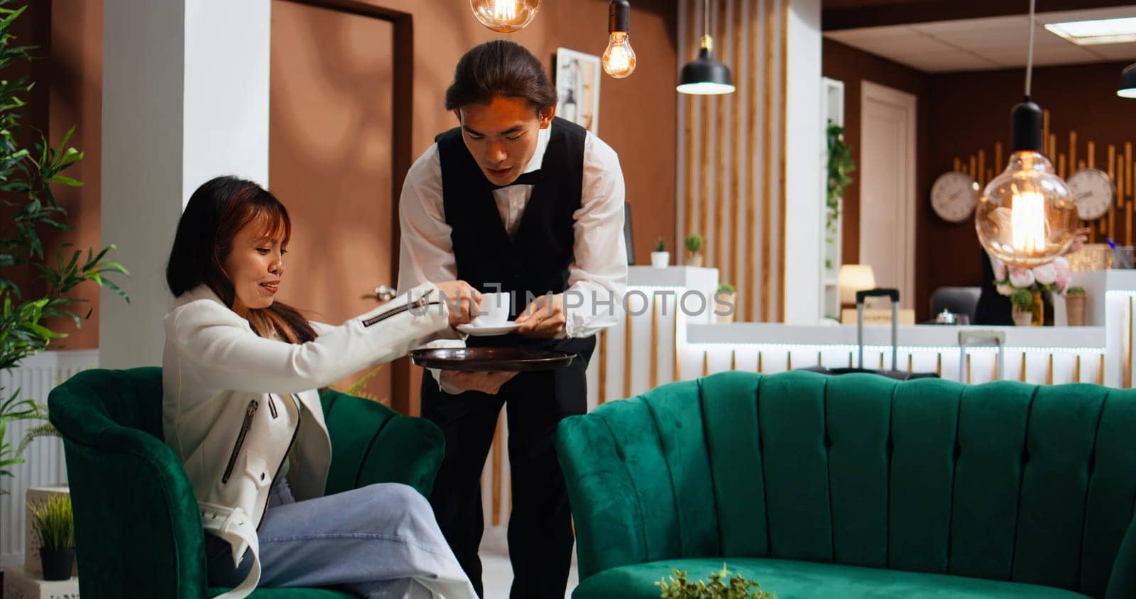 Customer ordering coffee and paying with credit card, waiter serving drink and holding pos terminal to receive payment. Asian woman receiving luxurious services from hotel staff. Handheld shot.