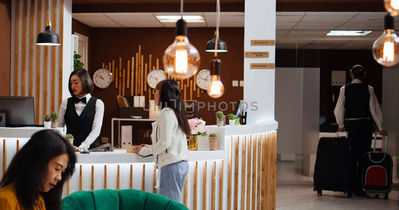 Hotel staff providing luxury concierge services for client arriving at front desk, helping with trolley bags and registering process. Asian woman confirming online room reservation for check in.