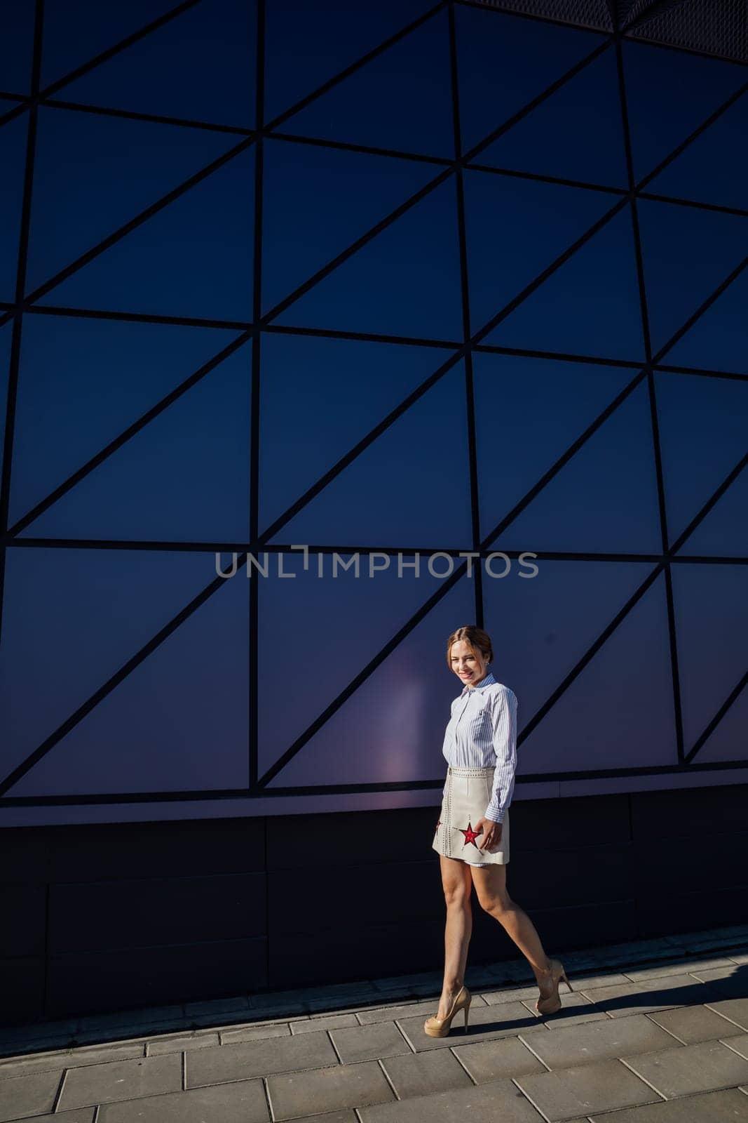 a woman walks near the glass wall of a building walk on the street by Simakov