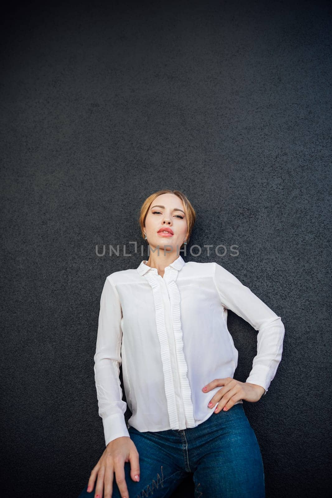 beautiful woman in a white blouse stands against a dark wall