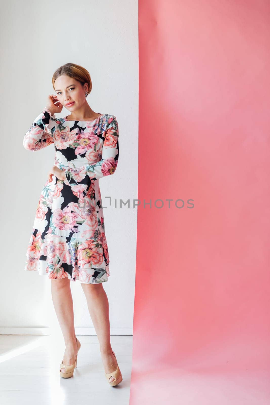 woman in a floral dress stands against a white pink wall