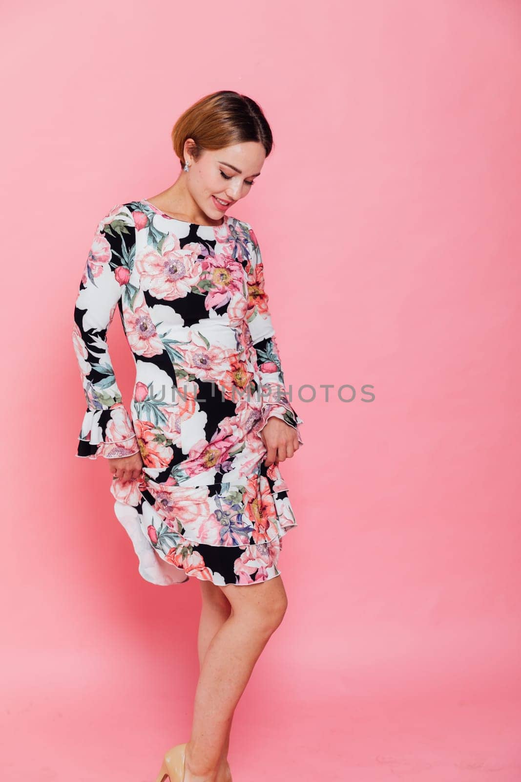 woman in a floral dress stands against a pink wall