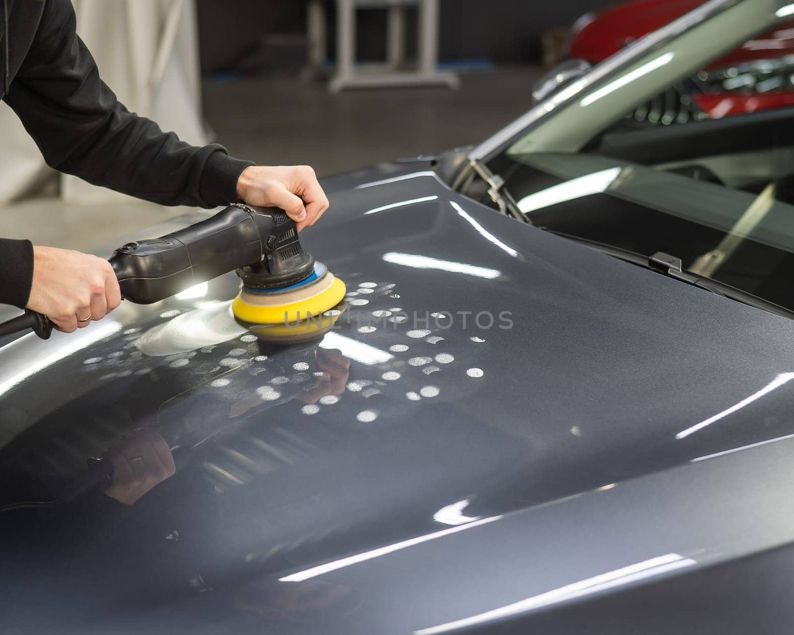 A mechanic polishes the surface of the hood of a gray car