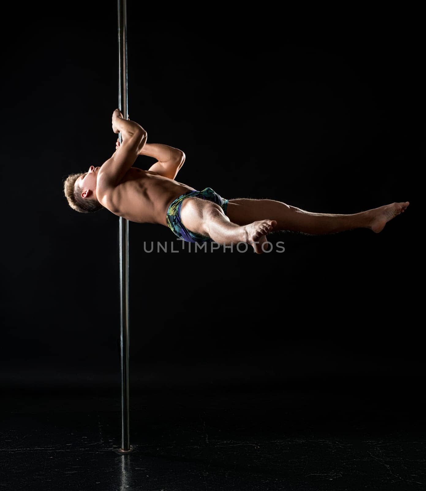 Male pole dance. Photo of strong guy dancing in studio