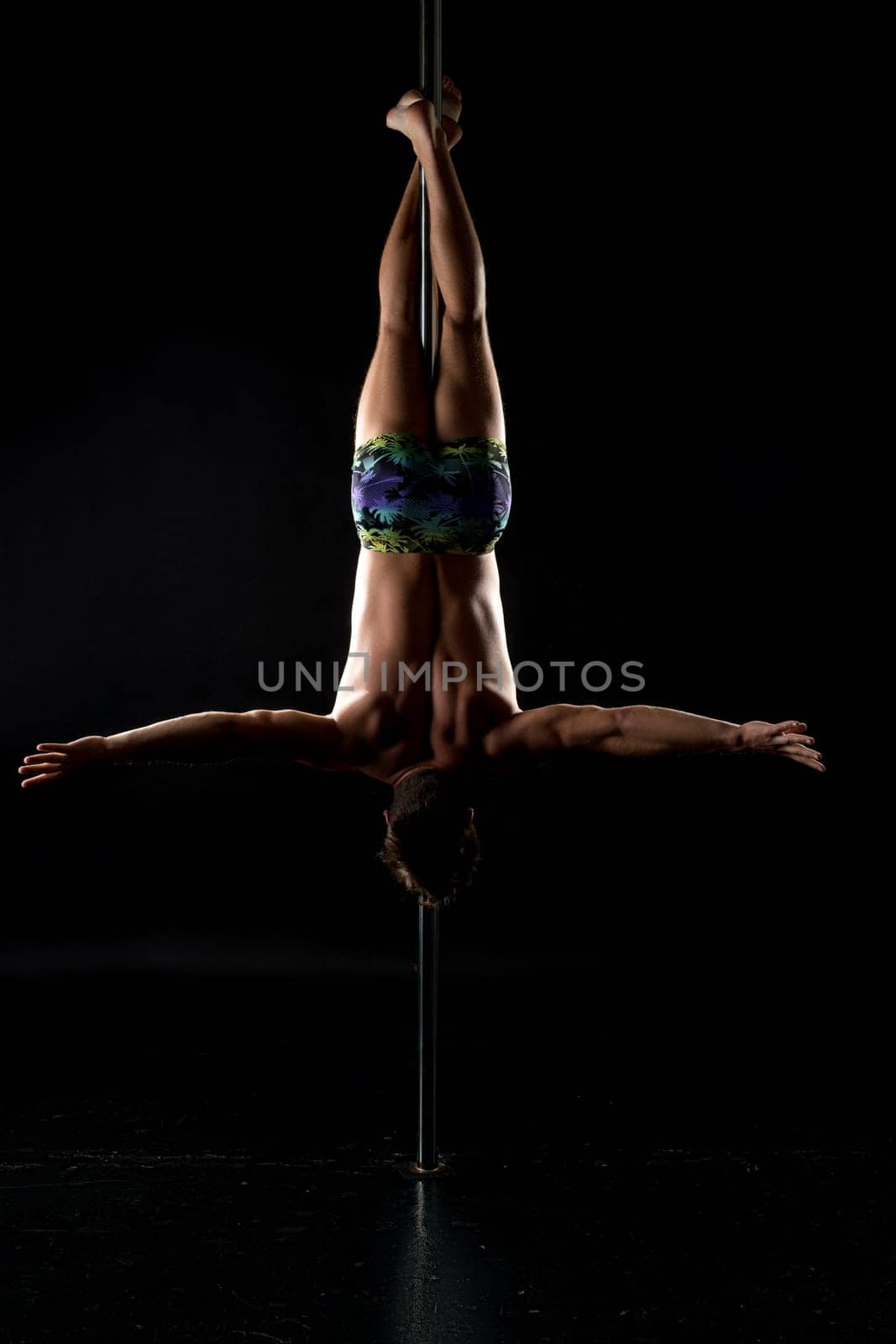 Pole dance. Image of strong man hanging upside down