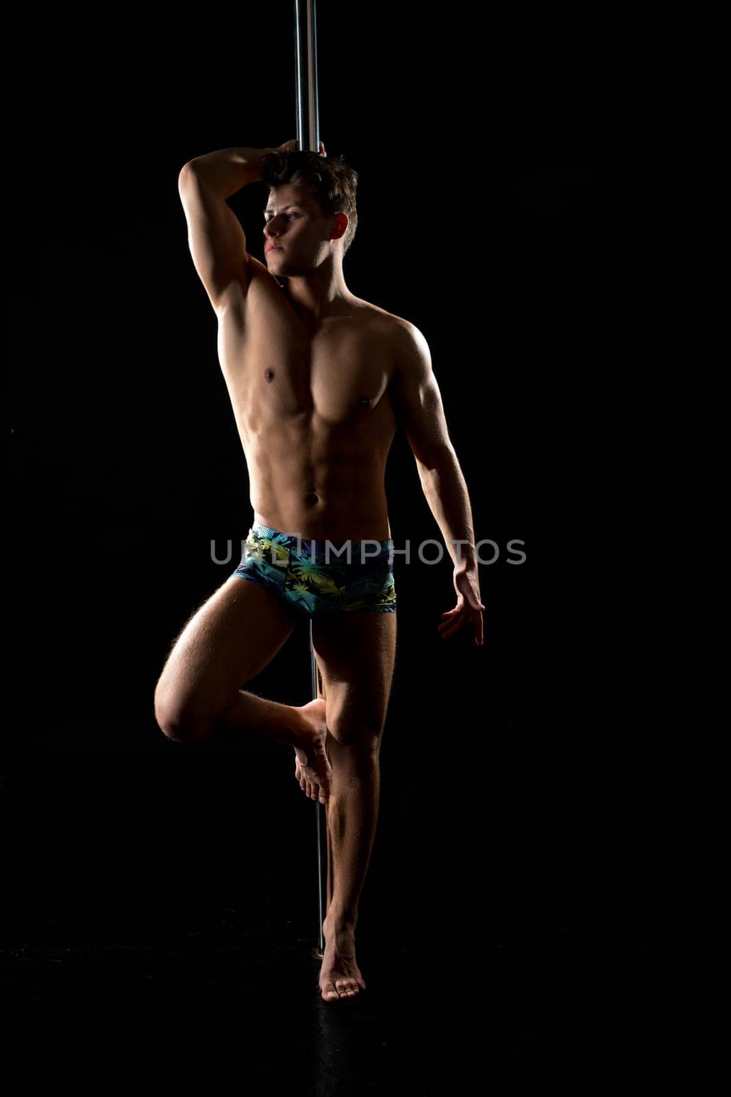 Male pole dance. Photo of muscular man posing at camera