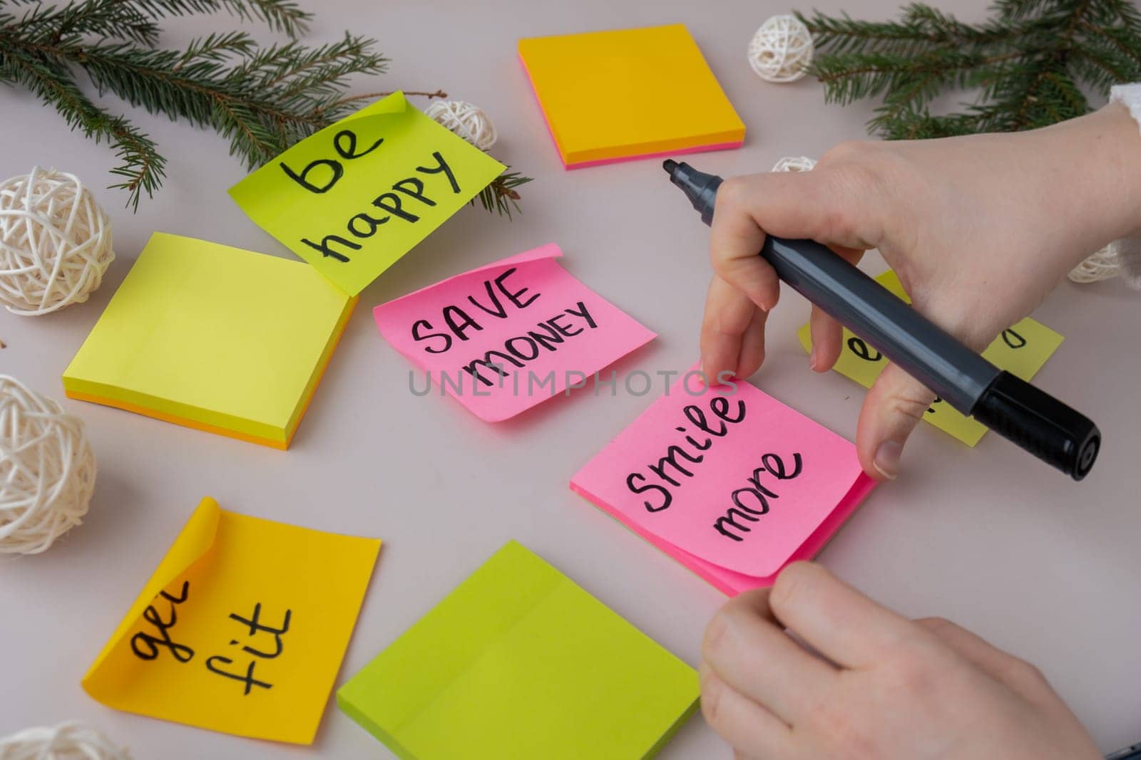 Unrecognizable woman writing new year's resolutions on colorful sticky notes. Making promises for new year, setting goals. Creating vision board motivation