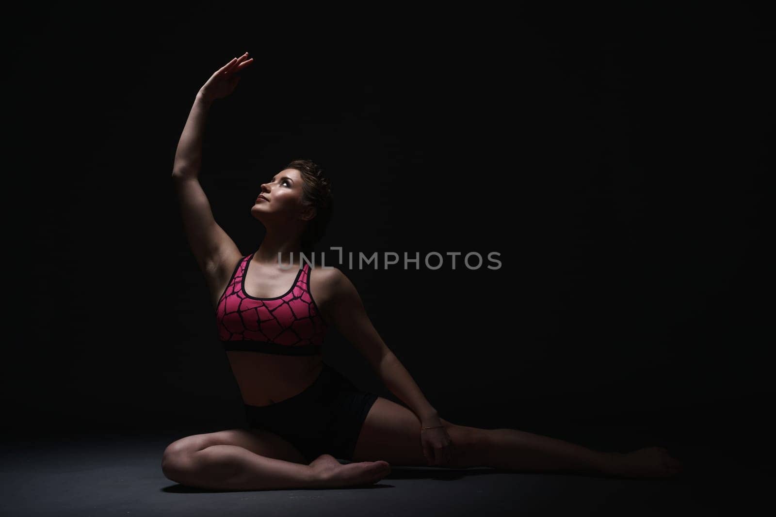 Studio photo of graceful brunette exercising in dark