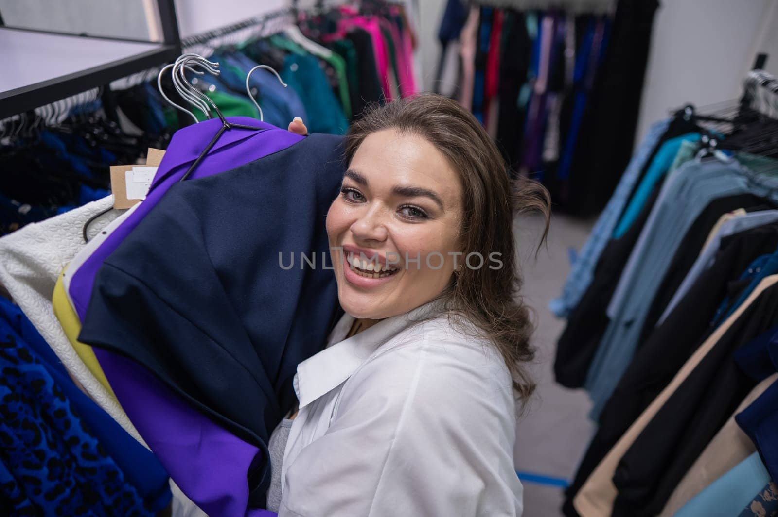 Top view of a chubby-cheeked woman holding an armful of clothes in a plus size store