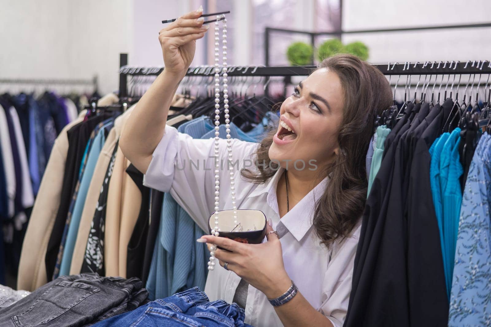 Happy fat woman fooling around and pretending to eat a pearl necklace with Chinese chopsticks in a clothing store for large people. by mrwed54