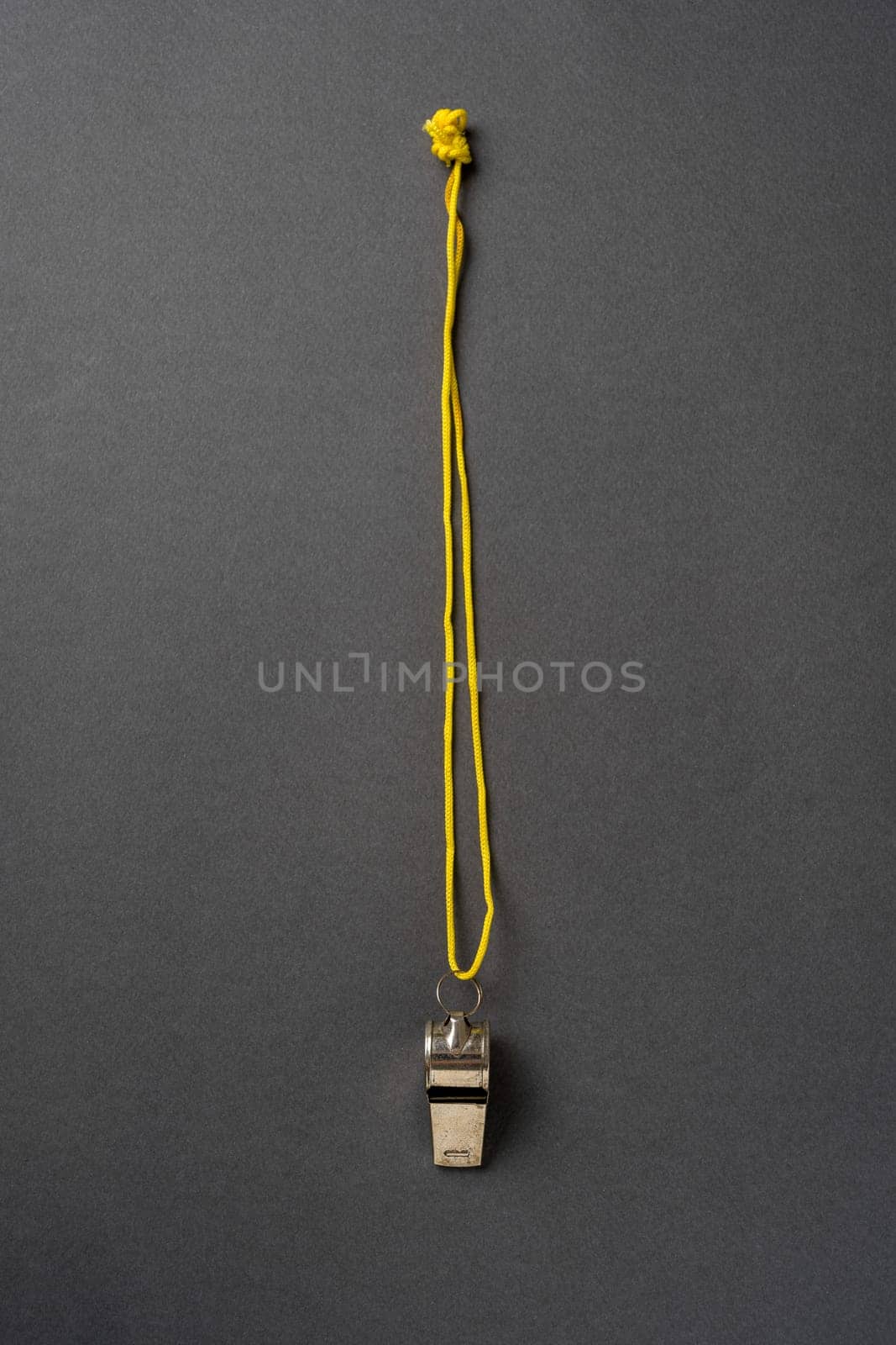 Top view of metal whistle with yellow string on dark gray background by Sonat