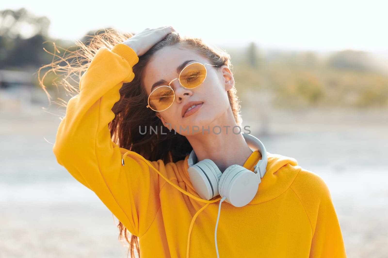 stylish woman in yellow sweater and sunglasses enjoys music with headphones on sunny day