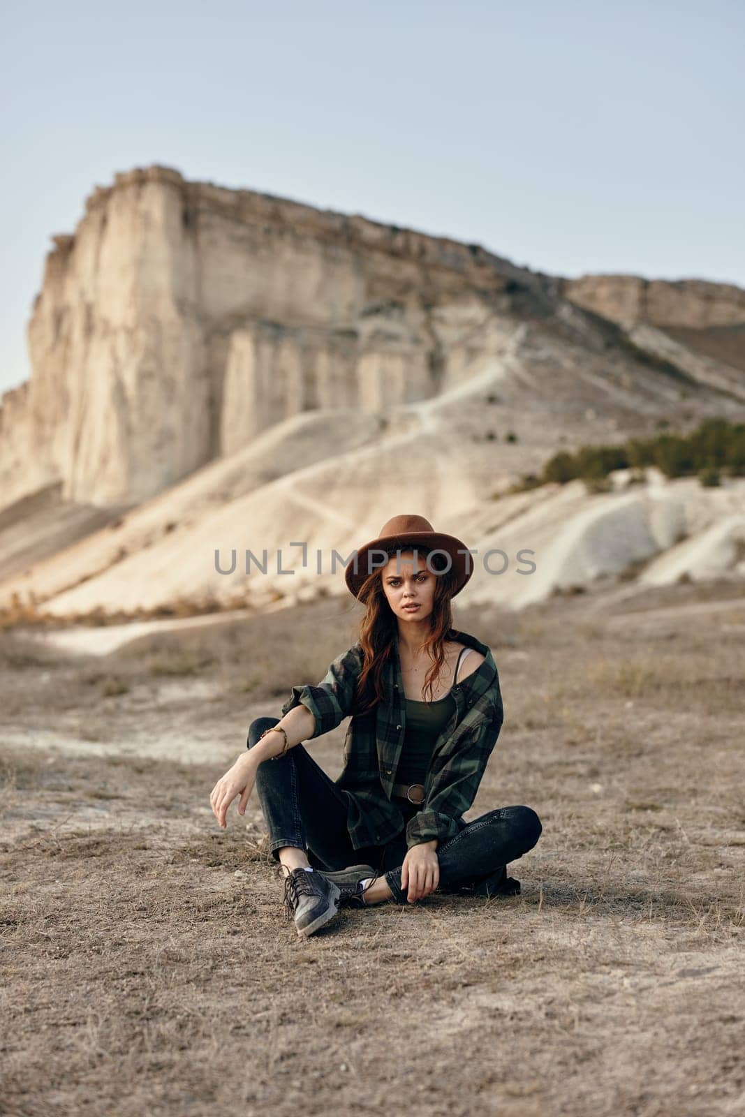 Woman in hat sitting in front of desert rock formation under the sun