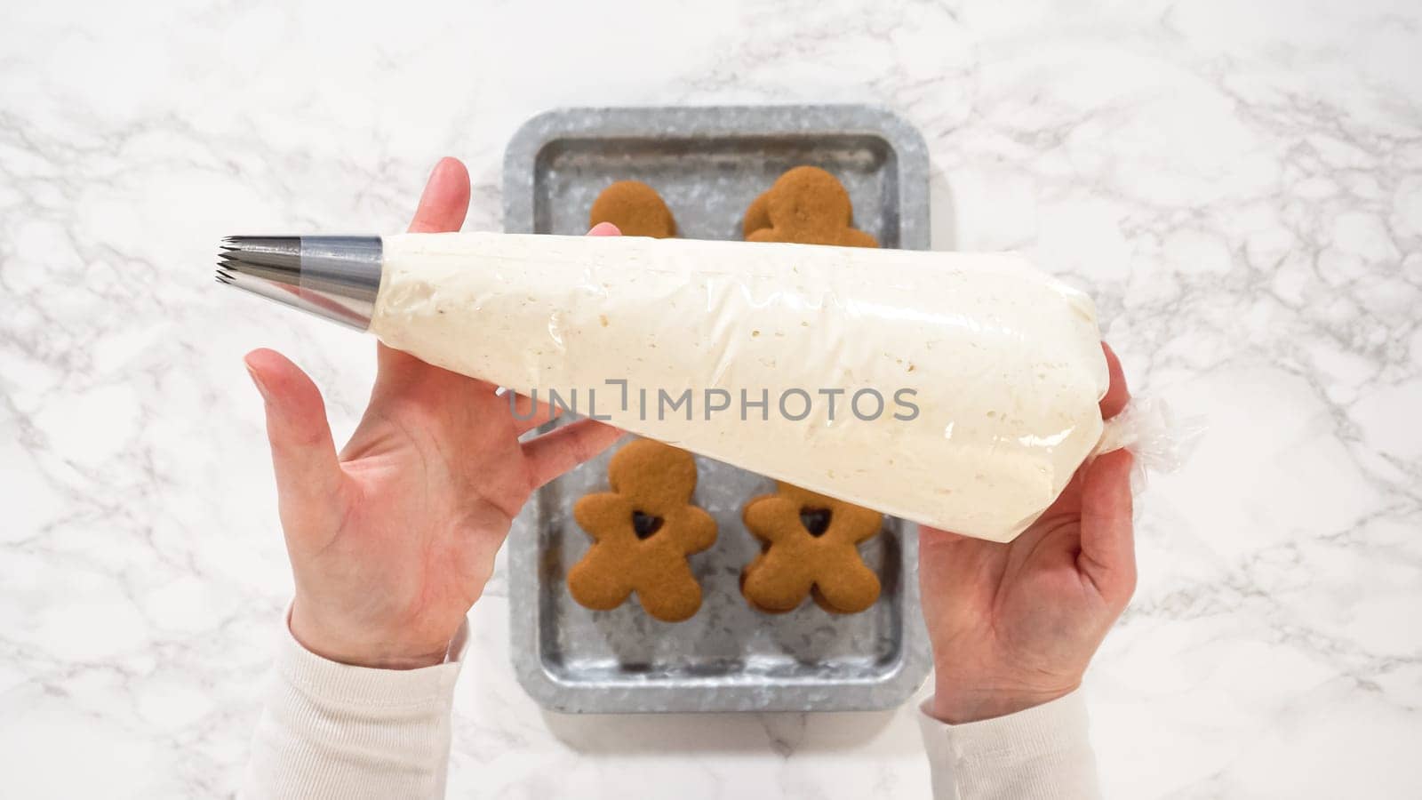 Flat lay. Gingerbread cookies await their second halves on a marble surface, each meticulously piped with buttercream to craft delightful sandwich treats. The precision of the piping adds a festive touch.