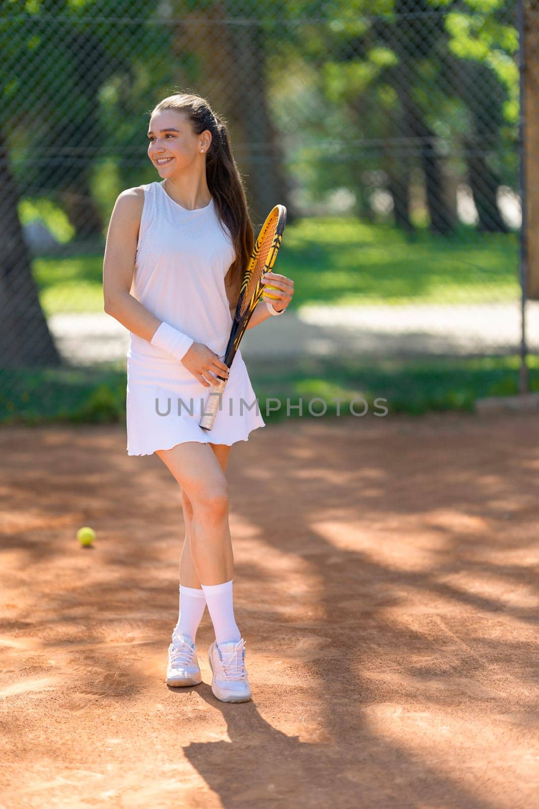 A woman is standing on a tennis court holding a tennis racket. She is wearing a white dress and white socks