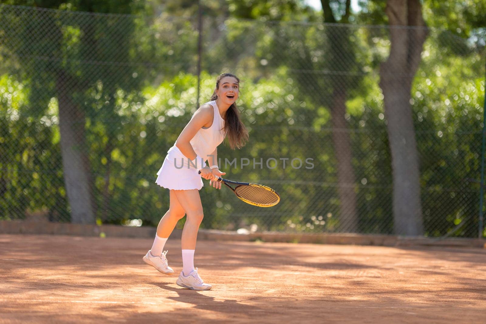 A woman is playing tennis on a clay court. She is wearing a white skirt and a white top