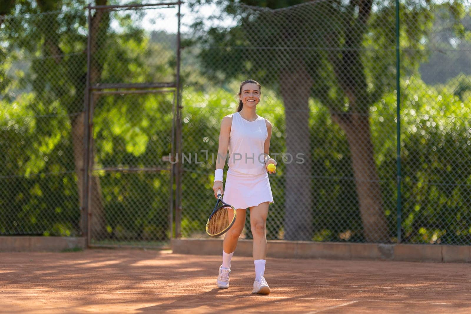 A woman is playing tennis on a court. She is holding a tennis racket and a tennis ball