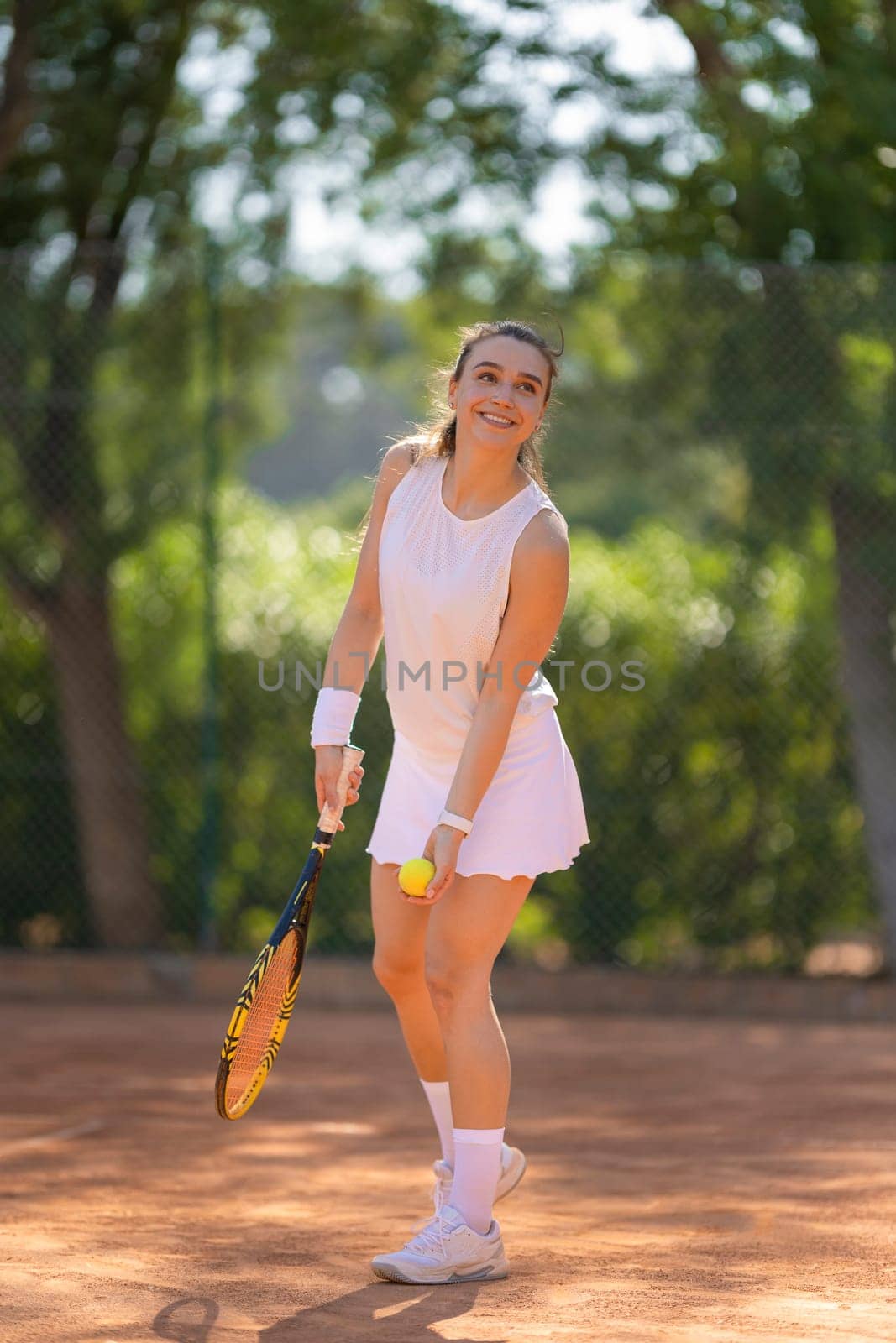 A woman is playing tennis on a court. She is wearing a white dress and holding a tennis racket