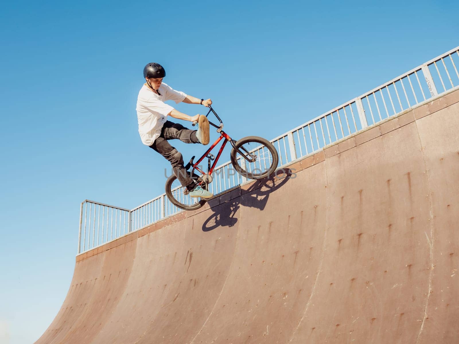 BMX bicycle rider flying and doing stunt Can-Can in wooden quarter pipe. Skilled BMX freestyler athlete jumping and doing aerial trick Can-Can in street wooden half-pipe ramp park