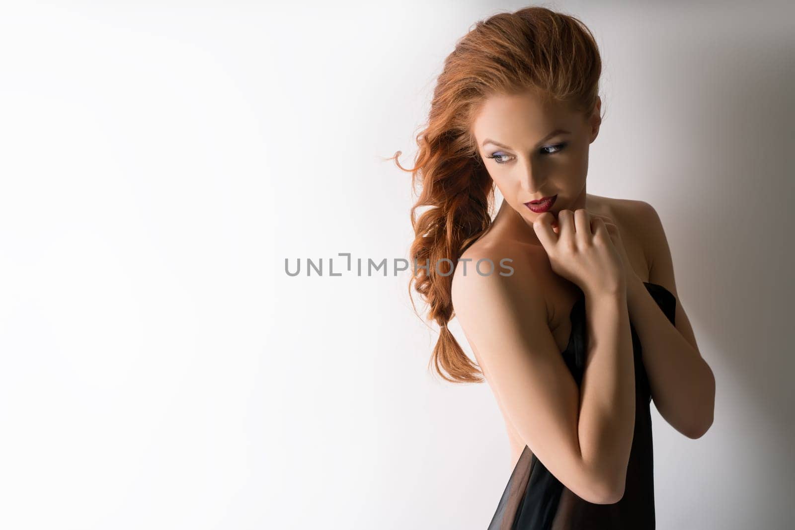 Portrait of beautiful red-haired woman presses her hands to face