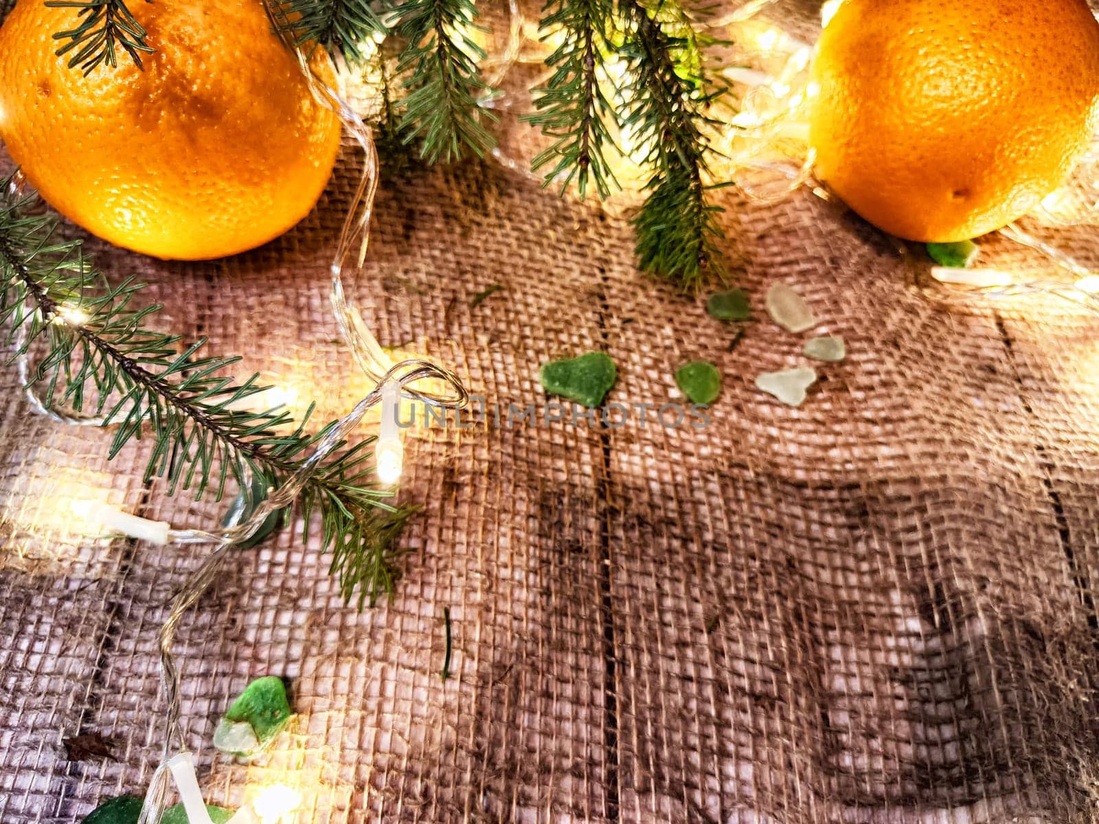 Festive decoration with a bouquet and branches of spruce, bright glowing garlands, burlap, oranges. Background for Christmas and New Year. Abstract texture, frame, place for text, copy space