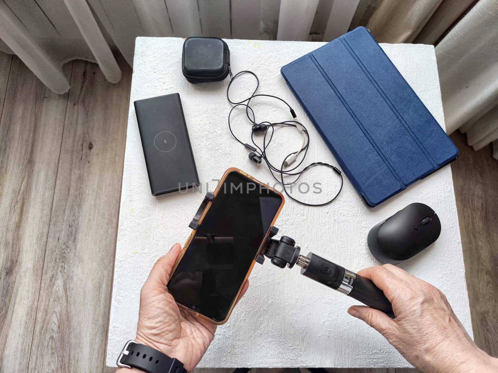 A set of useful blogger devices and hand of female blogger. A neatly organized desk featuring a smartphone, earphones, and various tech gadgets