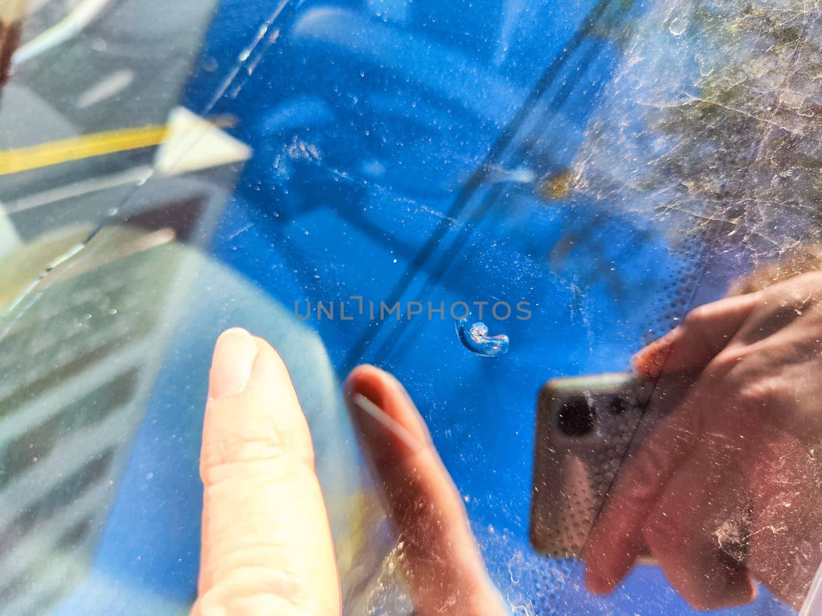 A hand points to a small chip on the driver-side window of a parked car, highlighted in bright daylight