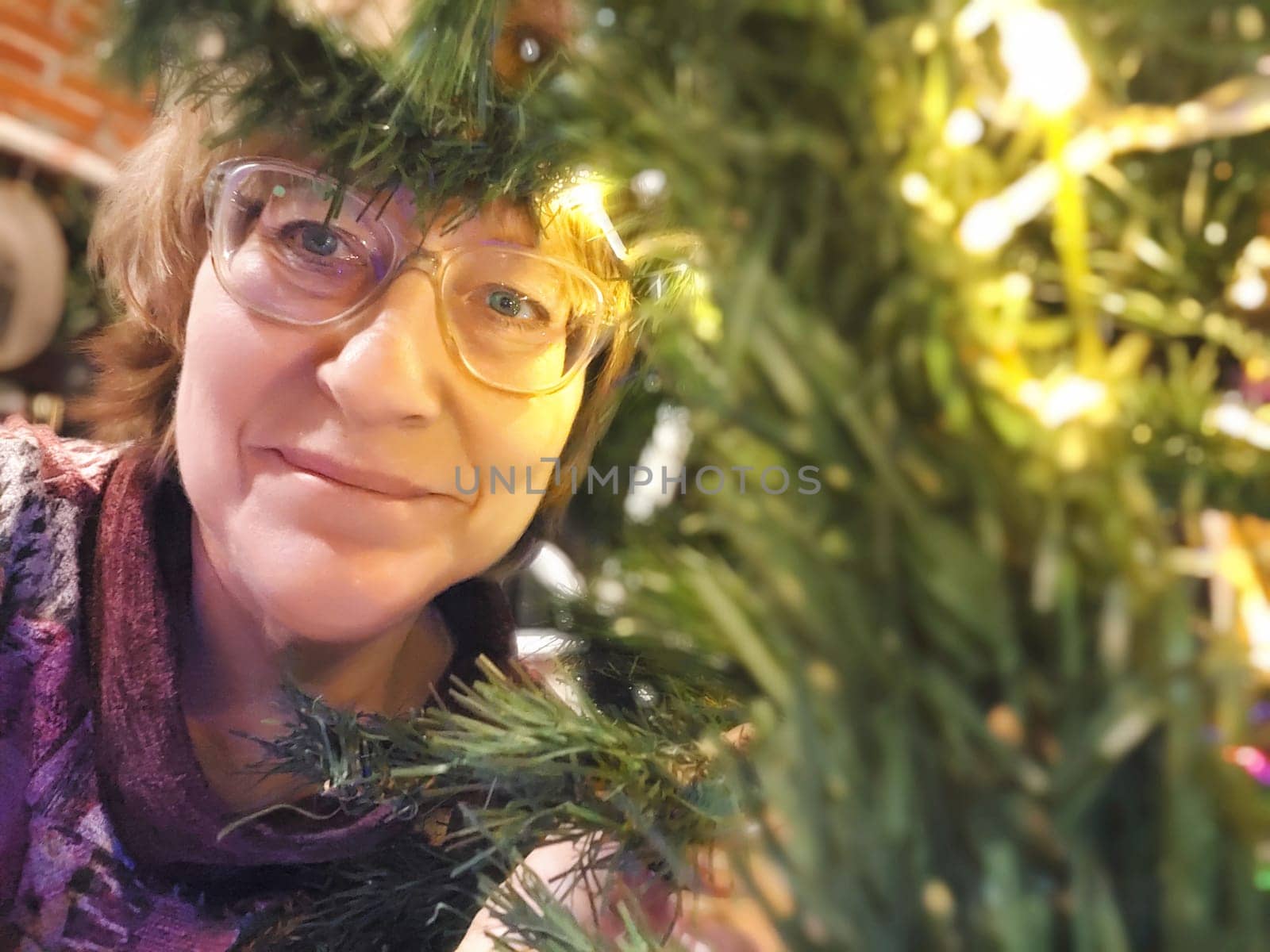 A close-up portrait of middle-aged woman smiling as she poses inside a Christmas tree. Partial focus, blurring, graininess
