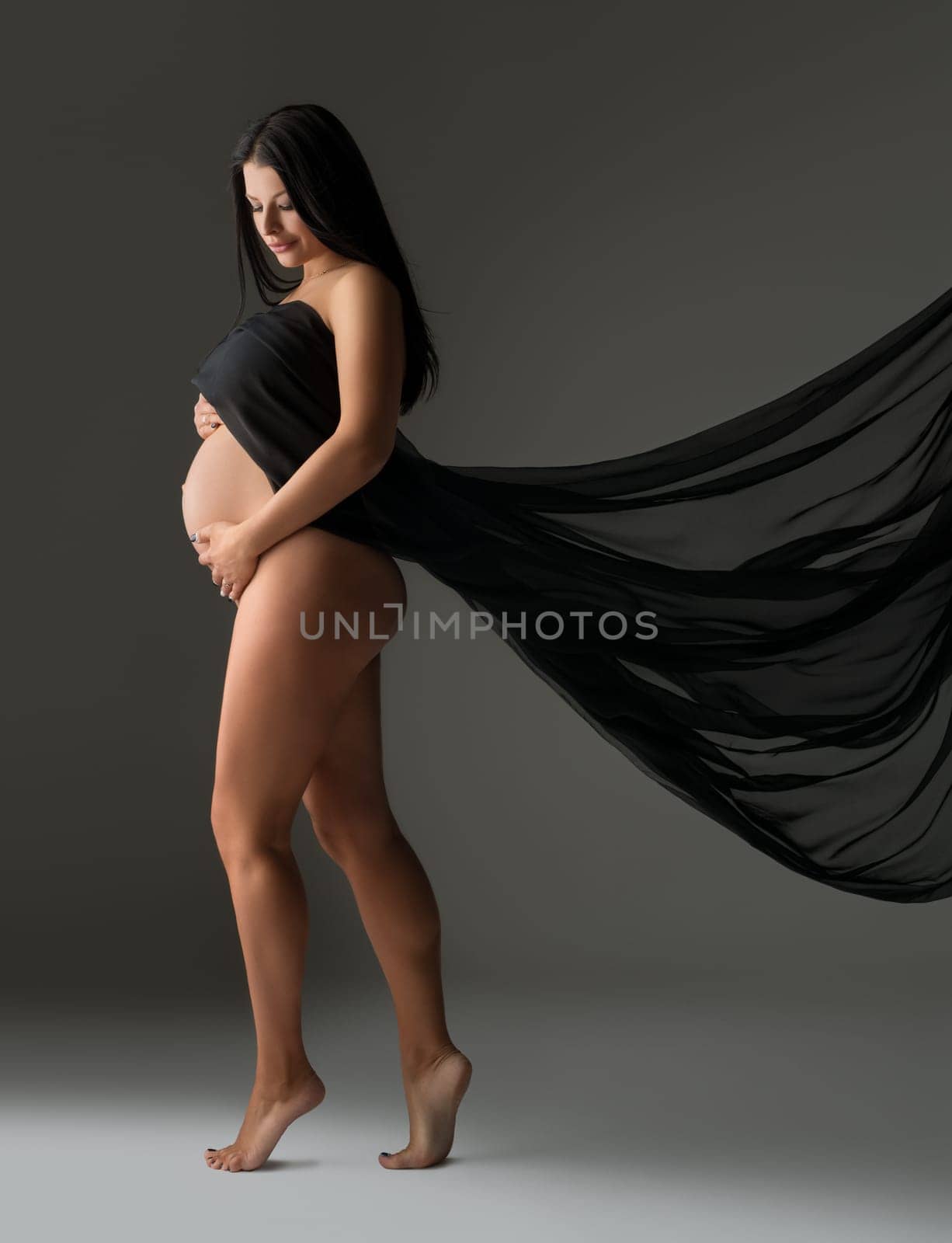 Elegant pregnant woman posing nude with flying cloth