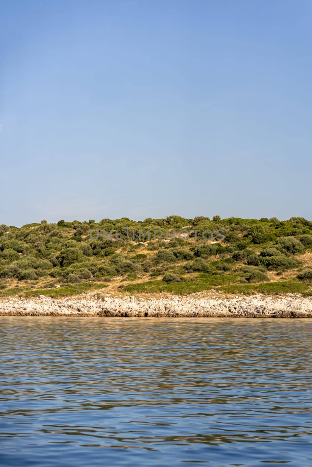 Rocky coast with green trees of Dugi Otok island, ripples on surface of blue water in Adriatic Sea, Croatia