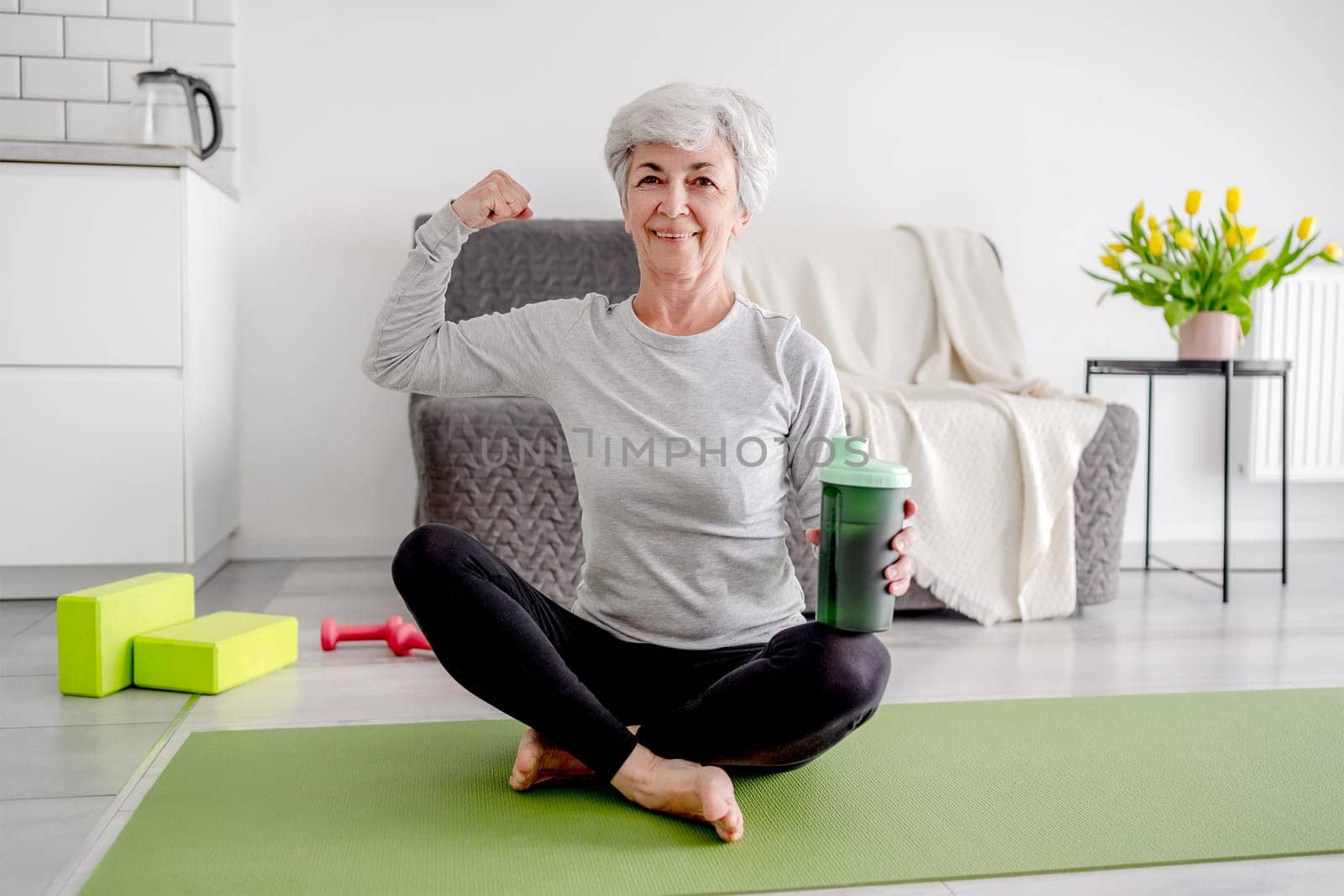 Cheerful Elderly Woman Looks At Camera Showing Her Bicep by tan4ikk1