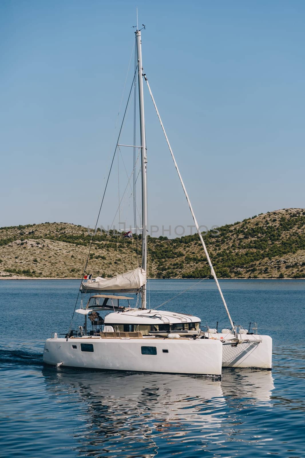 Modern yacht off hilly coast of Dugi Otok island, white boat in blue Adriatic Sea water, Croatia