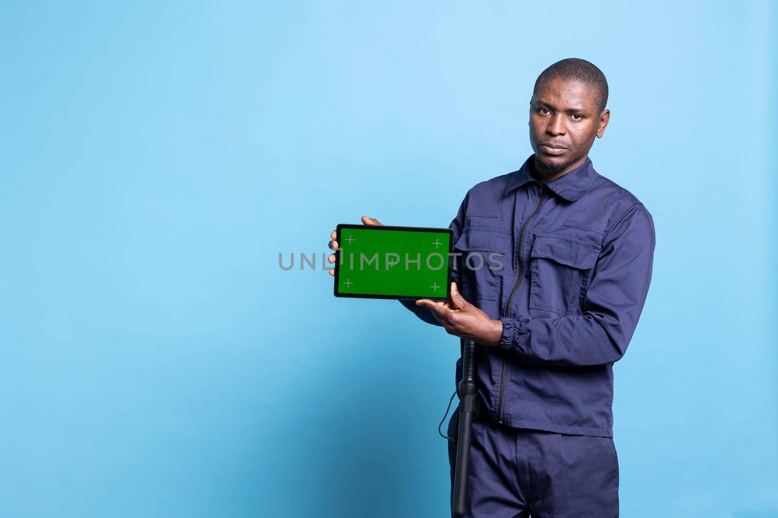 Security guard using a tablet to present an isolated greenscreen on camera, wearing his work uniform and smiling. Confident agent showing mockup screen on device in studio.