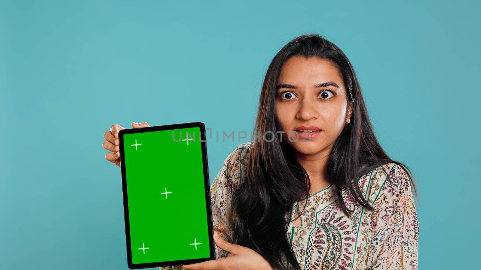 Person doing influencer marketing using isolated screen tablet, studio background. Indian woman holding empty copy space chroma key digital device, doing review, camera B