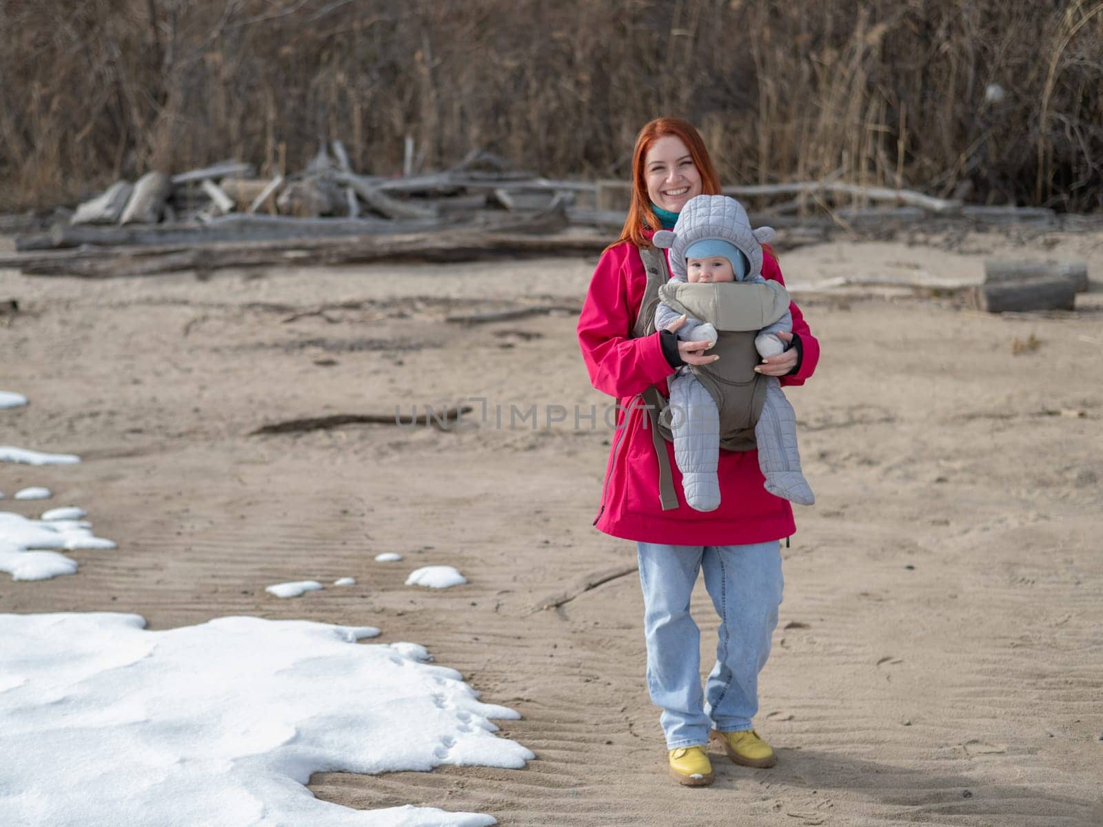 Caucasian red-haired woman walks with her son in an ergo backpack in nature in winter