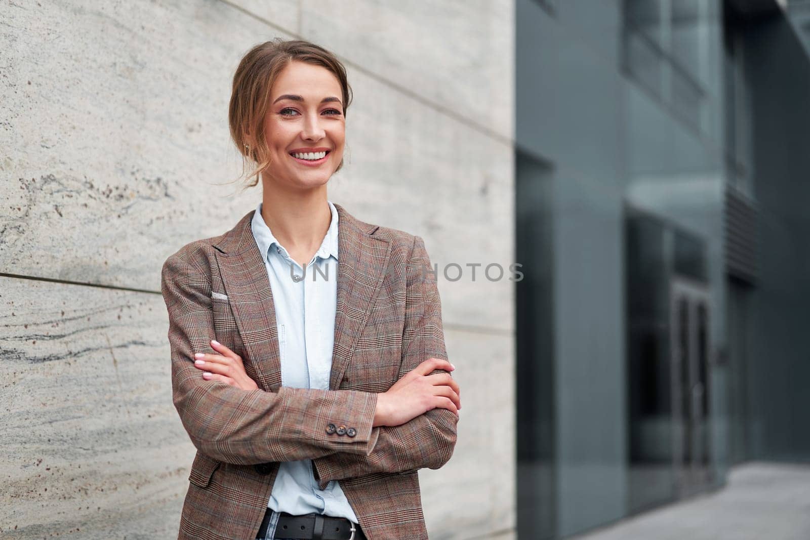 Portrait of smiling young businesswoman in formal standing arms crossed. Cheerful confident female entrepreneur looking at camera while standing outside modern office building.