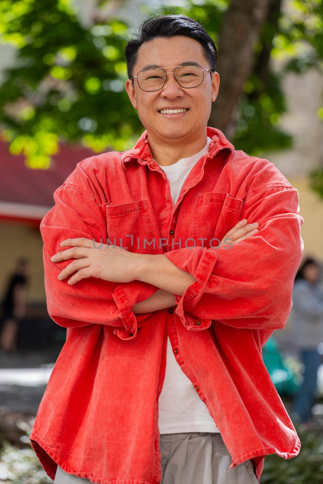 Portrait of happy Asian middle-aged man smiling friendly, glad expression looking at camera, resting, relaxation feel satisfied of good news outdoors. Chinese guy on urban city street. Town lifestyles