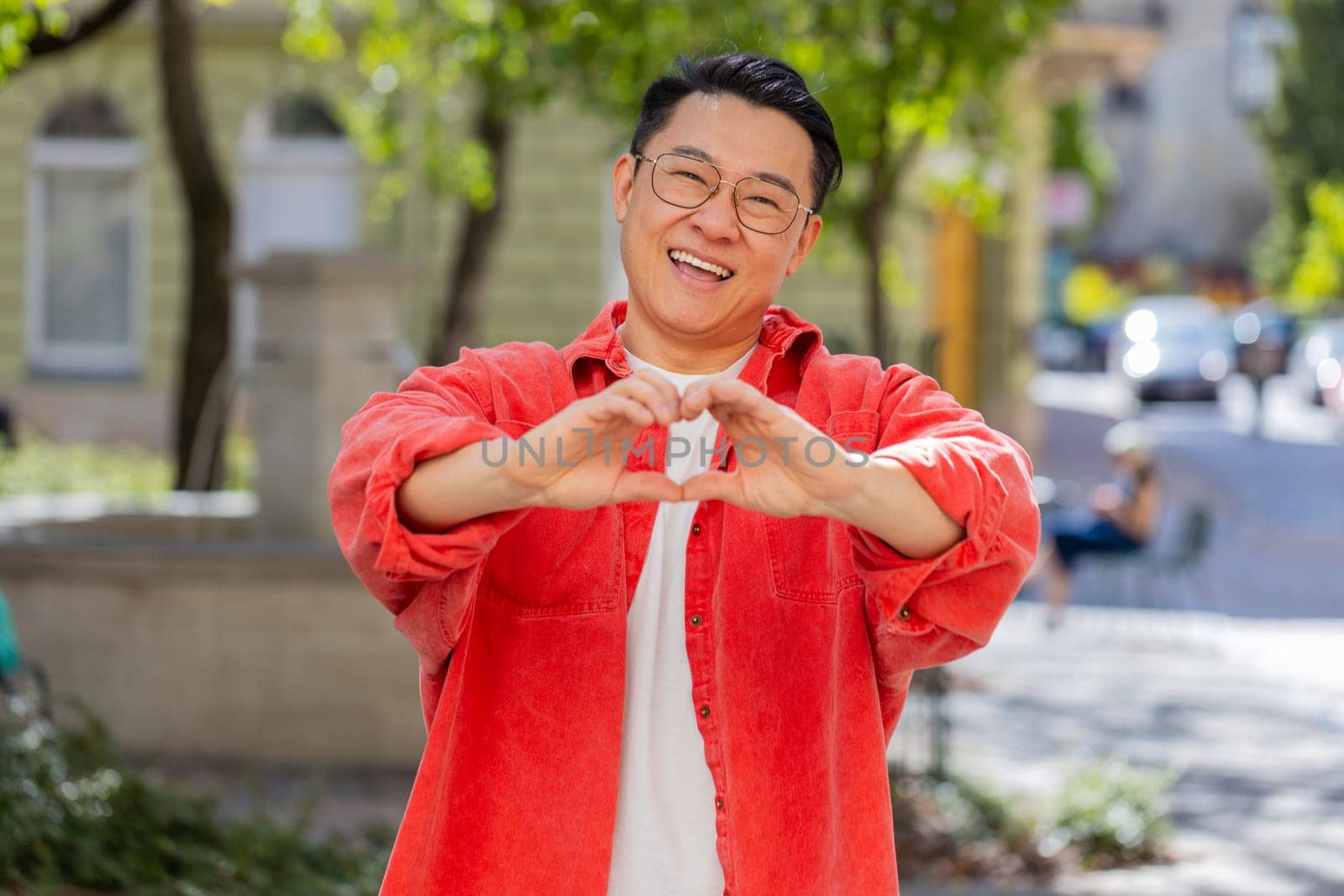 I love you. Asian middle-aged man makes symbol of love, showing heart sign to camera express romantic feelings, express sincere positive feelings outdoors. Charity, gratitude, donation. on city street