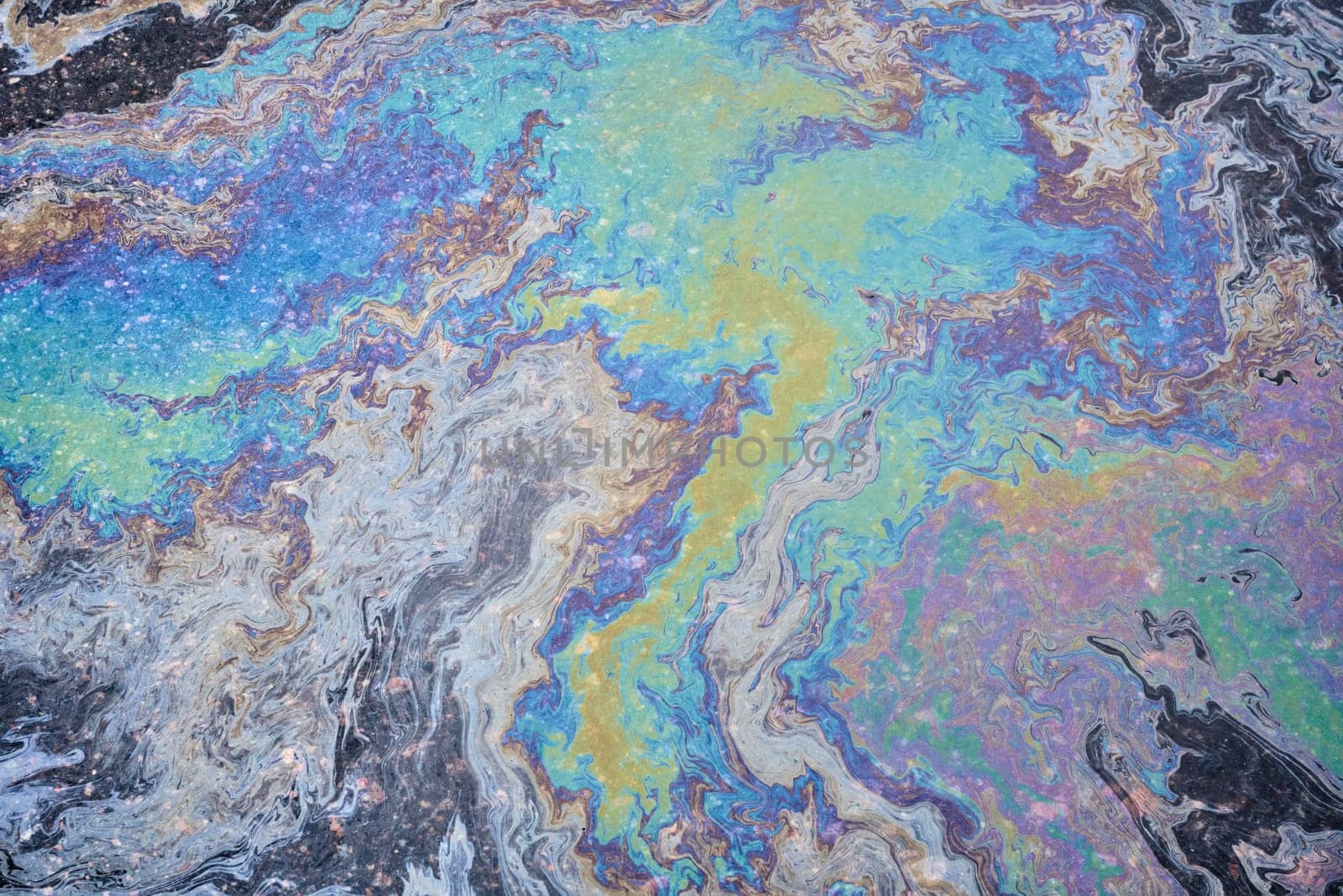A rainbow-hued slick of spilled engine oil and gasoline spreads across the asphalt surface, creating a vibrant textured backdrop.