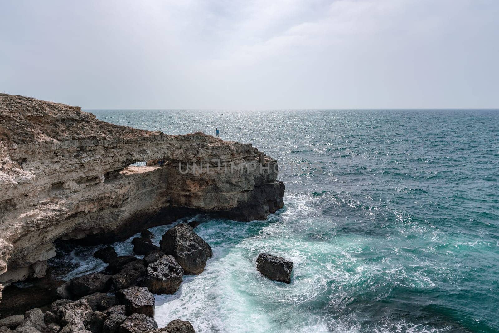 A rocky cliff overlooks the ocean, with the water crashing against the rocks. The scene is serene and peaceful, with the sound of the waves providing a calming atmosphere