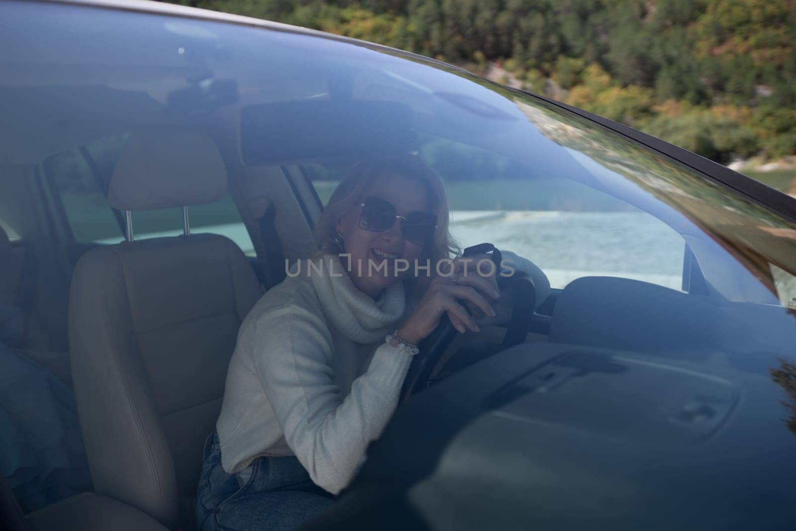 A blonde woman in a white sweater and jeans is driving. Happy woman sitting in a car with a white interior